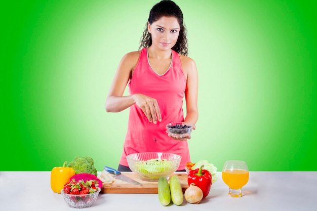 Mujer india agregando arándanos a una ensalada saludable