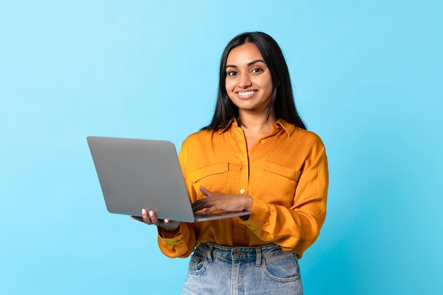 Mujer india alegre usando una computadora portátil posando sobre fondo azul del estudio