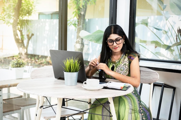 Mujer india con anteojos usando una computadora portátil