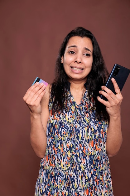 Mujer india estresada que tiene problemas con la tarjeta de crédito, compra productos en una tienda en línea, problema de pago en el sitio web de comercio electrónico. Persona enojada irritada que hace el pedido, usa un teléfono inteligente, busca productos