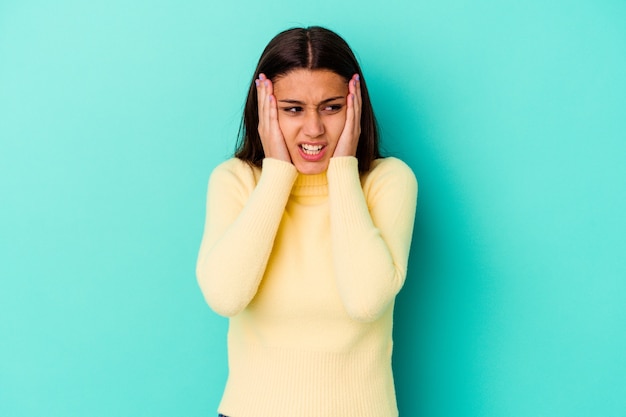 Foto mujer india joven aislada en la pared azul que cubre los oídos con las manos tratando de no escuchar un sonido demasiado fuerte.