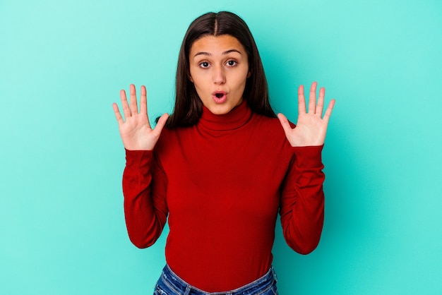 Mujer india joven aislada en la pared azul que tiene una idea, concepto de la inspiración.