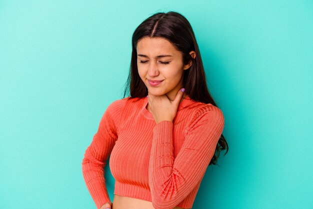 Foto la mujer india joven aislada en la pared azul sufre dolor en la garganta debido a un virus o una infección.