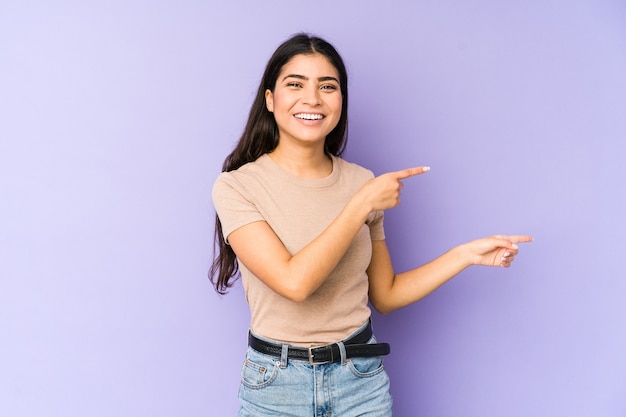 Mujer india joven aislada en la pared púrpura emocionada apuntando con los dedos índices de distancia.