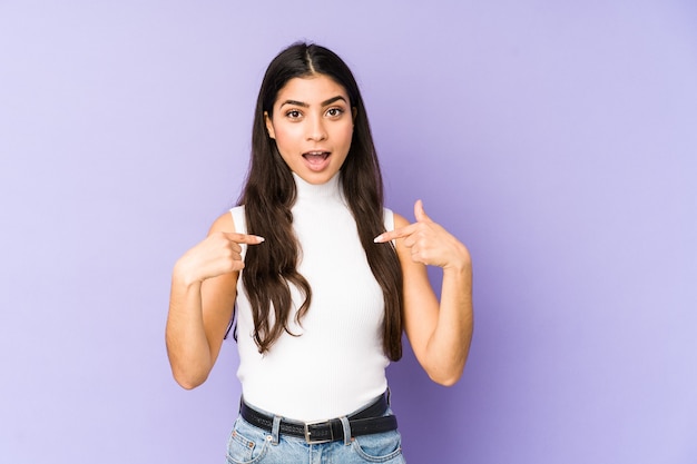 Mujer india joven aislada en la pared púrpura sorprendida señalando con el dedo, sonriendo ampliamente.