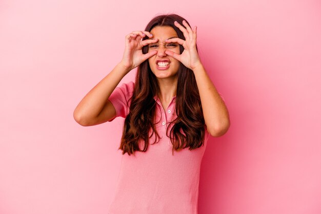 Mujer india joven aislada en la pared rosada que mantiene los ojos abiertos para encontrar una oportunidad de éxito.