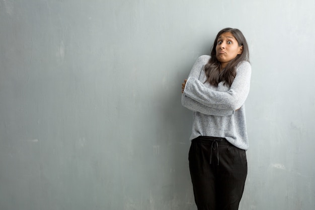 Mujer india joven contra una pared del grunge que duda y que encoge hombros