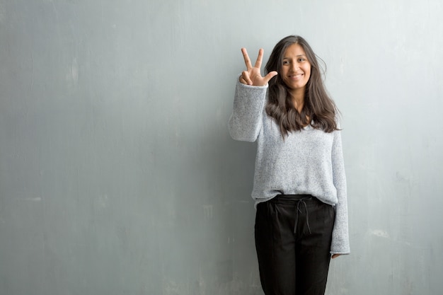 Mujer india joven contra una pared del grunge que muestra el número tres, símbolo de contar