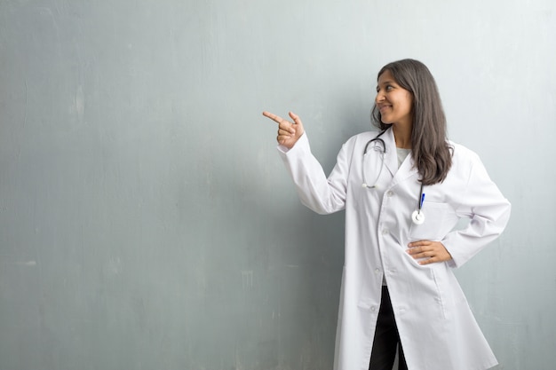 Mujer india joven del doctor contra una pared que señala al lado