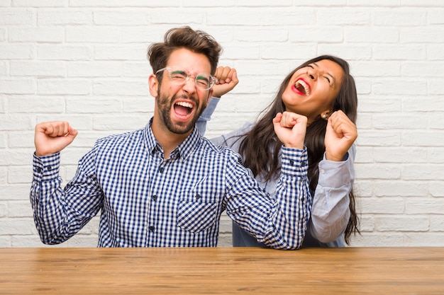 Mujer india joven y pareja de hombres caucásicos muy felices y emocionados, levantando brazos, celebrando una victoria o éxito, ganando la lotería