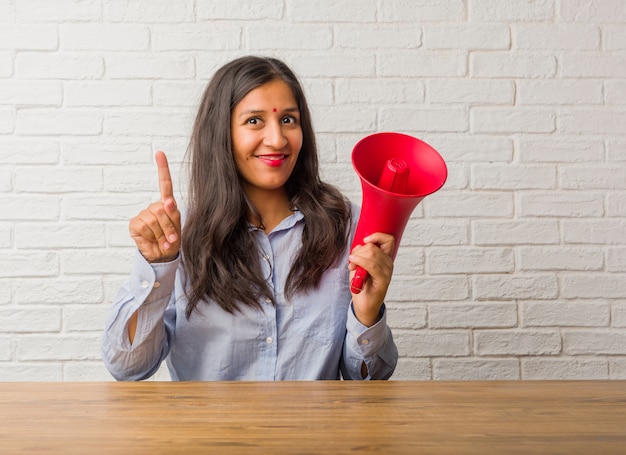 Mujer india joven que muestra el número uno, símbolo de contar, concepto de matemáticas, confiado y alegre. Sosteniendo un megáfono.