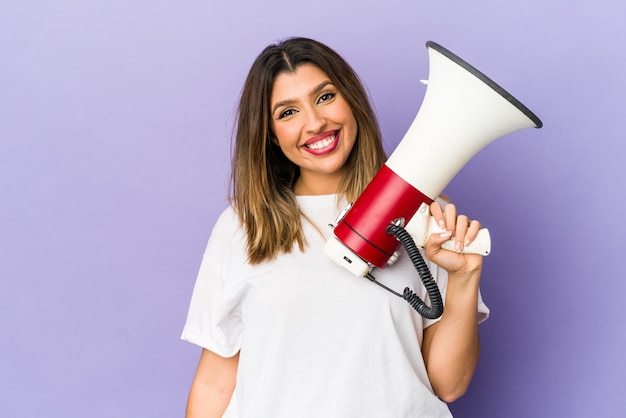 Mujer india joven que sostiene un megáfono aislado feliz, sonriente y alegre.