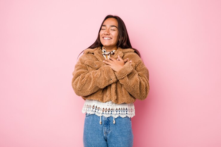 Foto mujer india joven de la raza mixta que lleva un coatlaughing corto de la zalea que guarda las manos en el corazón, concepto de felicidad.