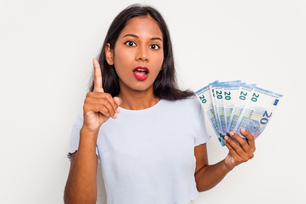 Mujer india joven sosteniendo un billete aislado en fondo blanco teniendo una idea