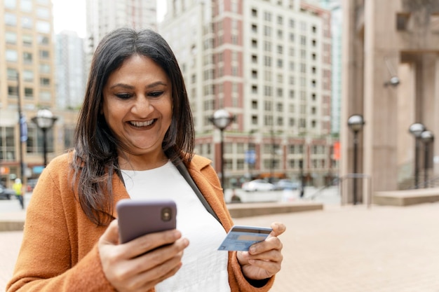 Mujer india madura con tarjeta de crédito y teléfono móvil recibe pago de pie en la calle