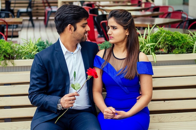 Mujer india morena de pelo largo con vestido azul con su guapo novio saliendo con un hombre dando rosa a su novia en la calle del centro de verano