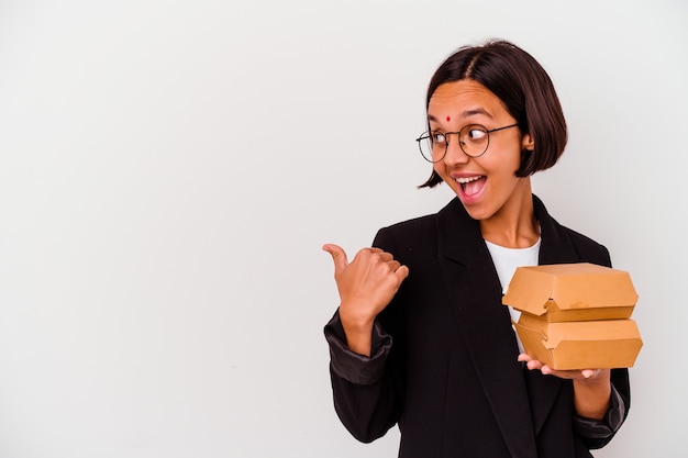 Mujer india de negocios joven comiendo hamburguesas puntos aislados con el dedo pulgar de distancia, riendo y sin preocupaciones.