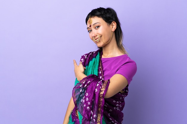 Mujer india en pared púrpura apuntando hacia atrás