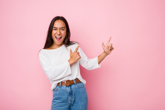 Mujer india de raza mixta joven apuntando con los dedos índice a un espacio en blanco, expresando emoción y deseo.