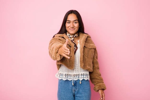 Mujer india de raza mixta joven con una mano de piel de oveja corta coatstretching en cámara en gesto de saludo.