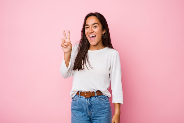 Mujer india de raza mixta joven que muestra el signo de la victoria y sonriendo ampliamente.