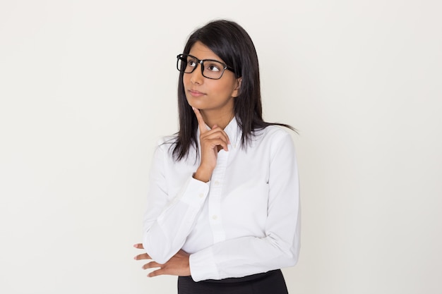 Mujer india en ropa formal y gafas apoyándose la barbilla en el dedo índice.