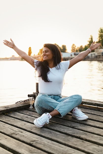 Mujer india sonriente despreocupada sentada en el muelle de madera