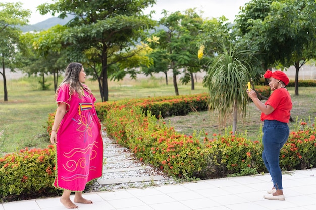 Mujer indígena bailando mientras su amiga toma fotos y videos con su celular en un parque de la ciudad