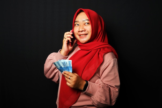 Una mujer indonesia recibió una llamada y tenía mucho dinero con una expresión feliz aislada de fondo negro