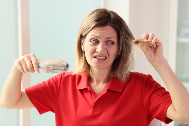 Mujer infeliz con cepillo para el cabello en la mano mirando su cabello, debilidad del cabello, pérdida de cabello y salud