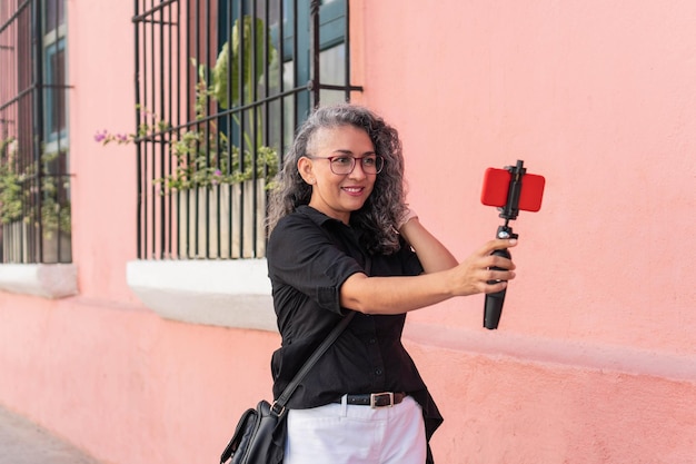 Mujer influyente latina sonriendo mientras transmite con su celular al aire libre en la calle