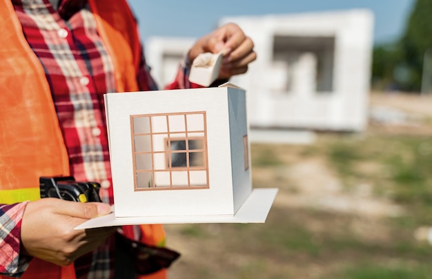 Mujer ingeniera y arquitecta trabajando con modelo de casa en el sitio de construcción.