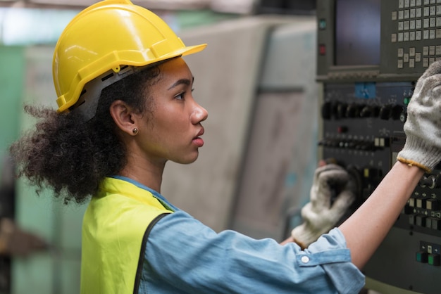 Mujer ingeniera asiática con casco amarillo que trabaja con máquina operativa en la fábrica Industrial