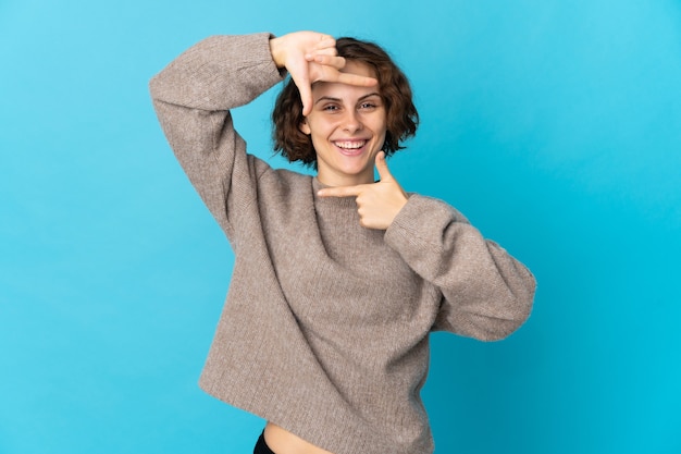 Mujer inglesa joven aislada en la cara que se centra de la pared azul. Símbolo de encuadre