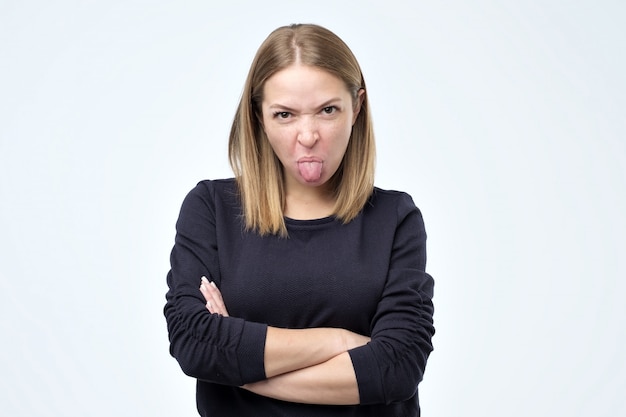 Mujer insatisfecha frunce el ceño, tiene una expresión repugnante, muestra la lengua