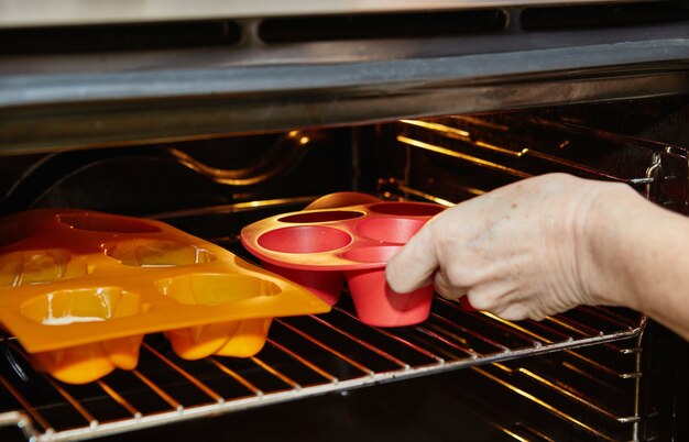 Mujer inserta moldes para muffins en el horno para hornear muffins de tomate secados al sol.