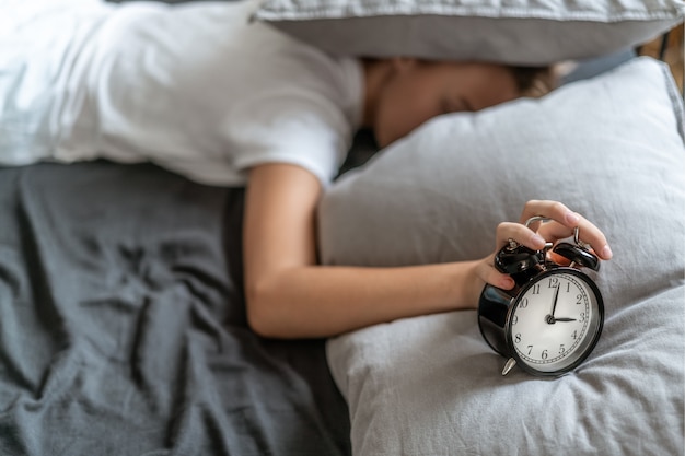 Mujer con insomnio acostada en la cama con la cabeza debajo de la almohada tratando de dormir.