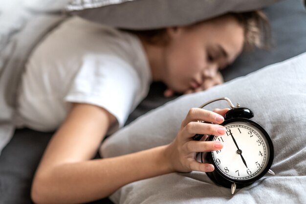 Mujer con insomnio acostada en la cama con la cabeza debajo de la almohada tratando de dormir.