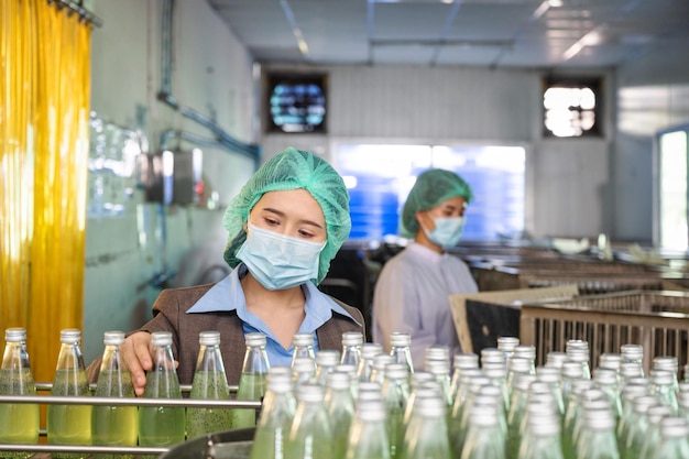 Mujer inspectora revisando una bebida de fruta embotellada en la línea de producción de transportadores en la fábrica de bebidas de procesamiento