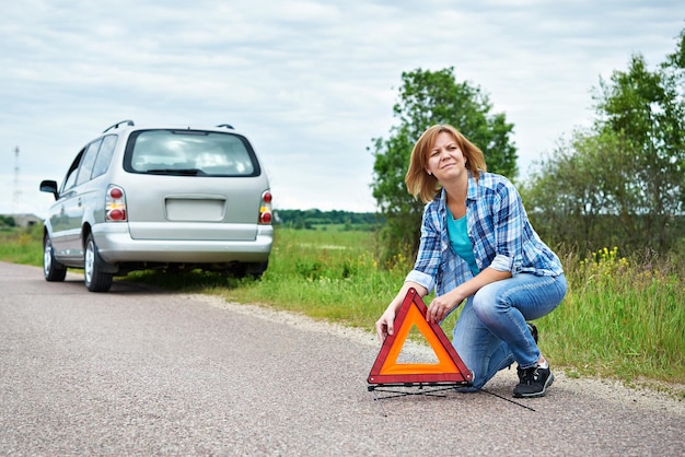 Mujer instalando una señal de emergencia en la carretera cerca del coche