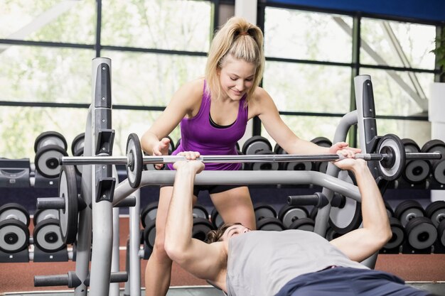 Mujer del instructor que ayuda al hombre atlético en el gimnasio del crossfit