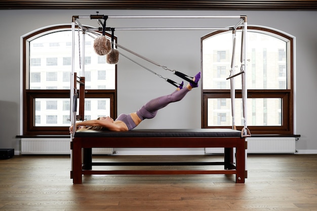 Mujer instructora de aeróbicos de Pilates en ejercicio físico en el reformador de cadillac, entrenamiento del sistema musculoesquelético en el simulador de reformador moderno.