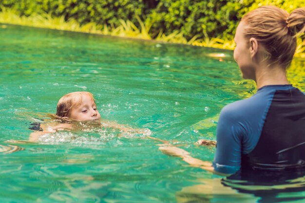 Mujer instructora de natación para niños está enseñando a un niño feliz a nadar en la piscina