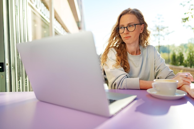 Mujer inteligente con gafas sentada en un café usando una laptop