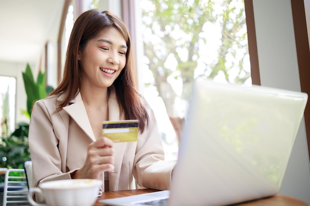 Mujer inteligente usa tarjeta de crédito para pagos de compras en línea por computadora portátil en la cafetería