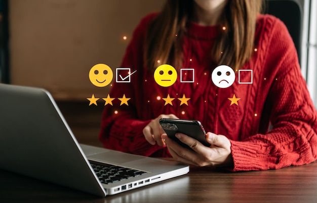 La mujer inteligente usa un teléfono inteligente y una tableta eligiendo la calificación de retroalimentación del icono de la cara de sonrisa feliz y la evaluación positiva de la salud mental de la experiencia de revisión del cliente