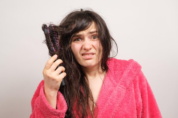 Una mujer intenta peinarse el cabello mojado enredado