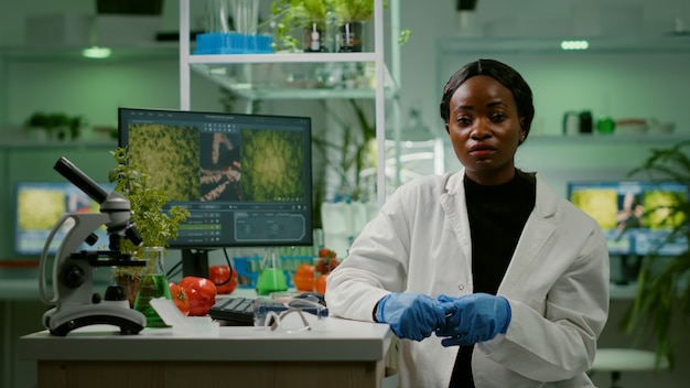 Mujer investigadora botánica explicando el experimento de botánica durante la reunión de videollamada en línea mientras está sentado en el laboratorio farmacéutico