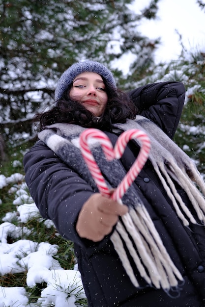 Mujer en invierno sosteniendo dos bastones de caramelo formando un corazón Feliz Año Nuevo Navidad