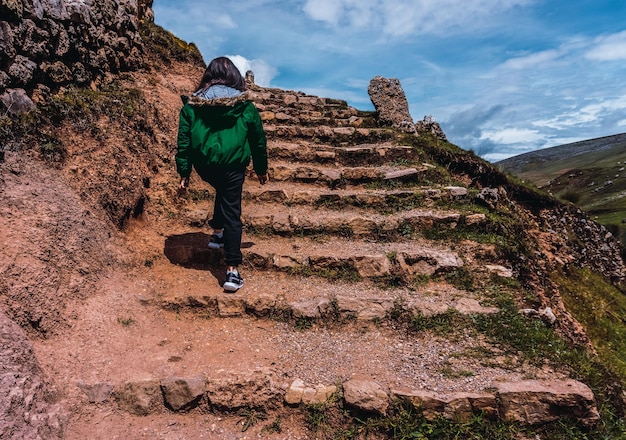 Mujer irreconocible con abrigo verde subiendo escaleras rústicas en San Pedro de Cajas Tarma Perú